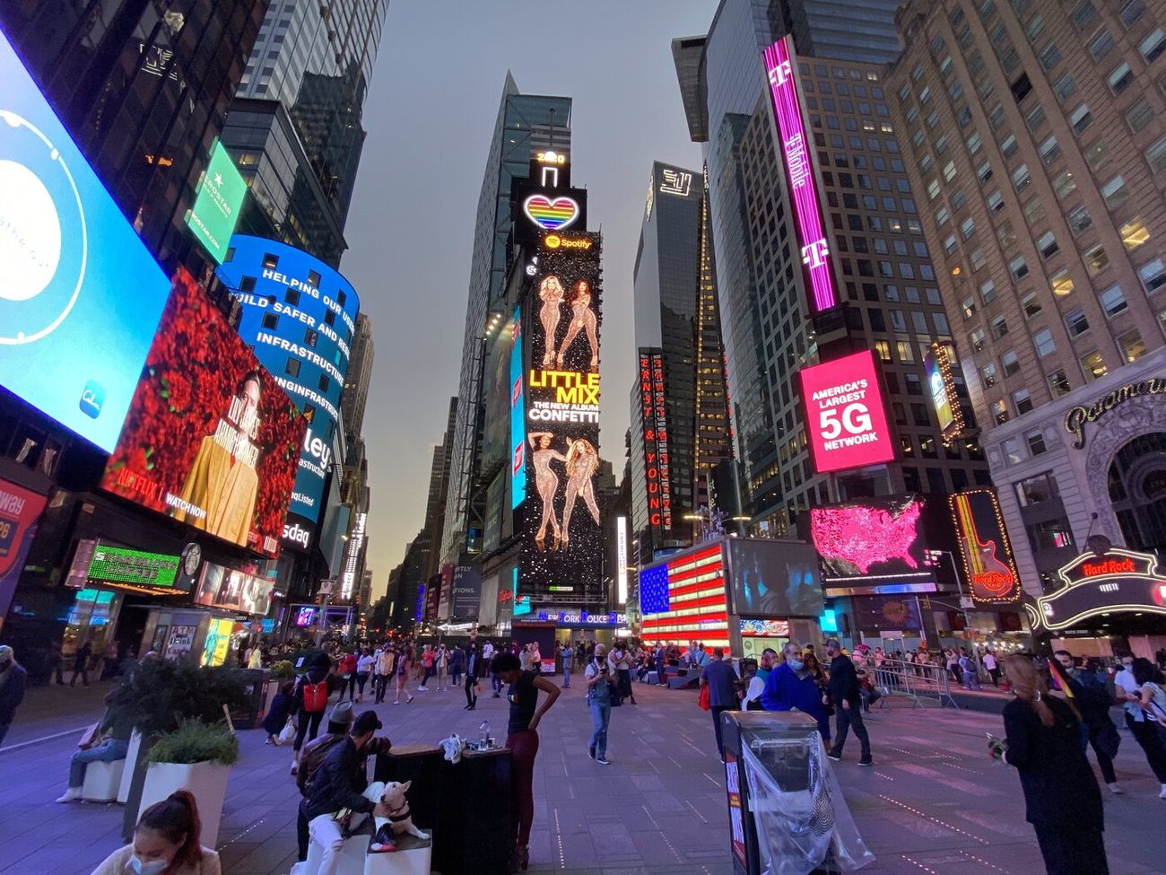 A crowd in Times Square at dusk beneath a wall of billboards, nobody looking up at any of it